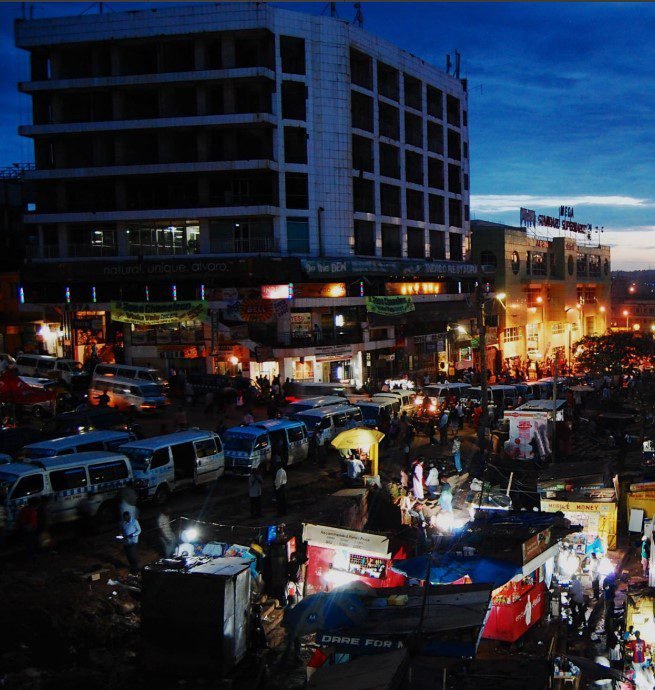 Busy street scene in Kampala at night with lights, people, and motorcycles.