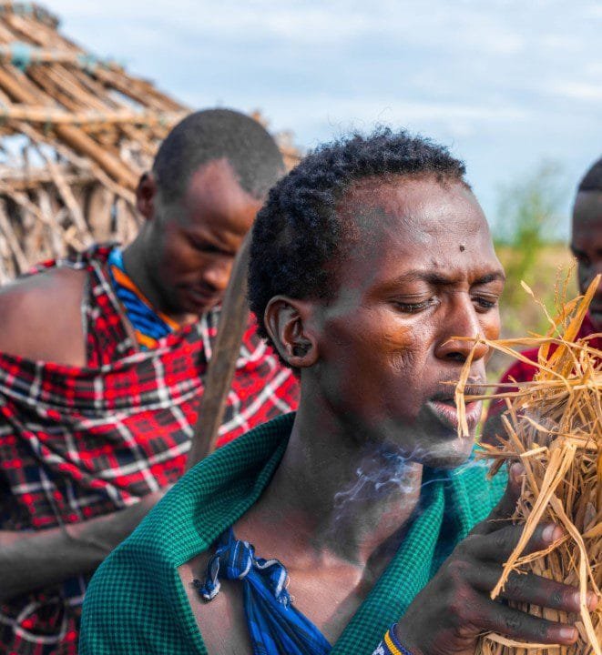 A traditional healer in Tanzania performing a spiritual ritual with fire, using herbs and cultural tools.