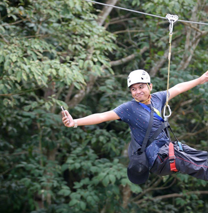 Person zip-lining through a lush green forest canopy in East Africa, surrounded by trees and scenic natural landscapes.